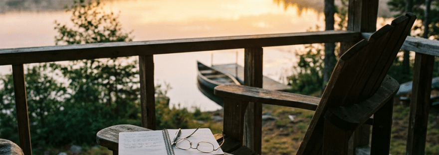 Wooden chair on porch overlooking lake at sunset with notebook and glasses