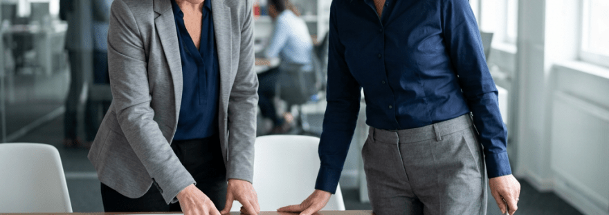 Two women in business attire discussing documents on a table in a modern office